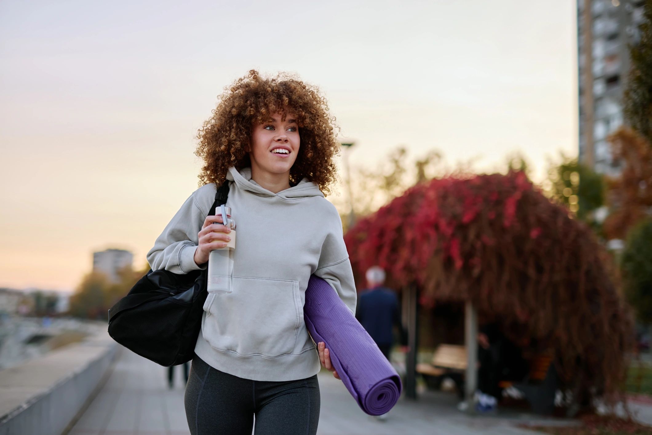 Woman walking after a workout carrying a yoga mat and gym bag